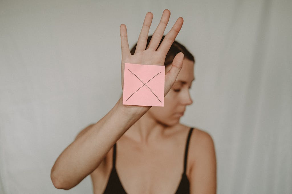 A woman holds up her hand with a pink sticky note displaying a cross symbol, conveying a clear message of refusal.