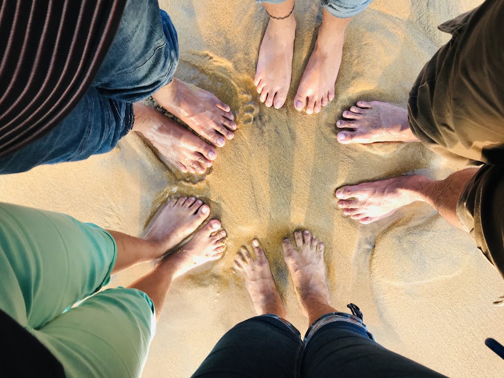 Aerial view of friends' feet forming a circle on a sunny sandy beach.