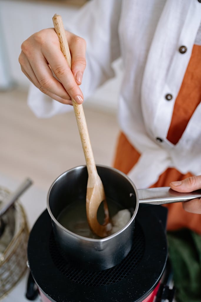 Close-up of hands stirring wax in a pot, showcasing DIY candle making.