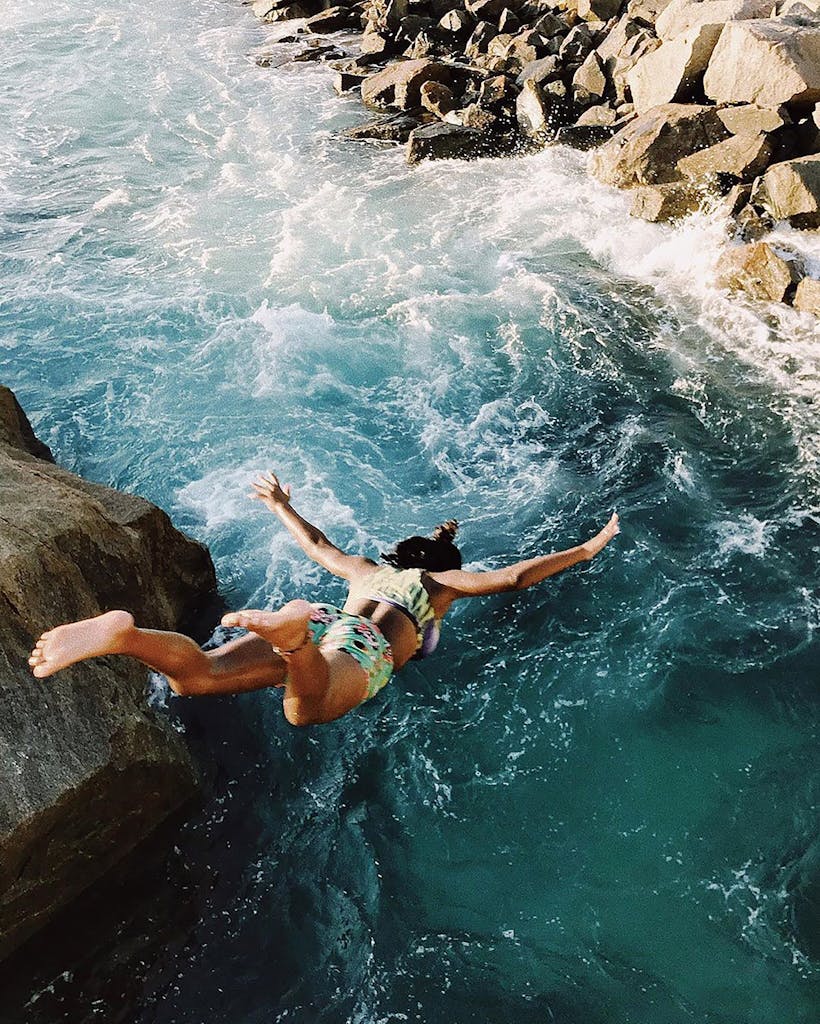A woman in a bikini jumps off a cliff into the ocean in Arraial do Cabo, Brazil.